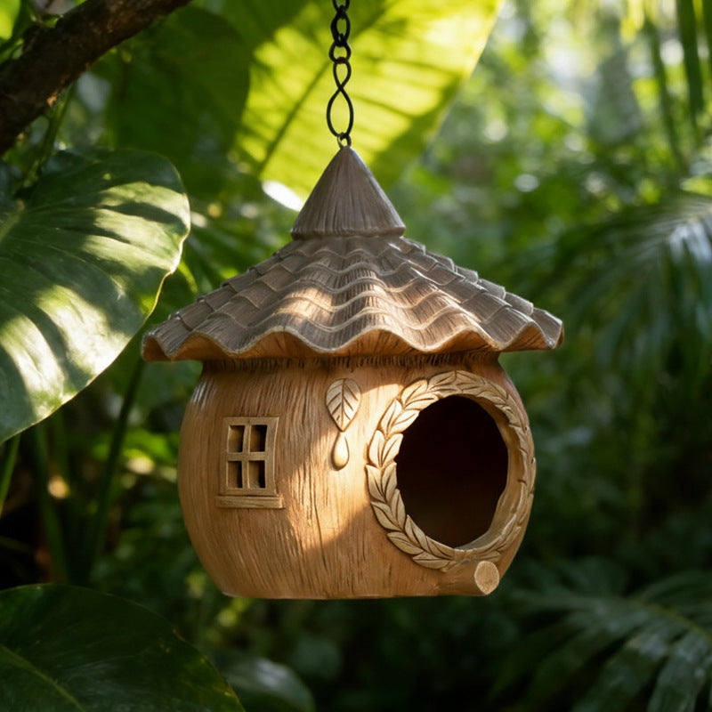 The Little Cottage Birdhouse — a hanging cottage-style birdhouse with a tiled roof among green leaves