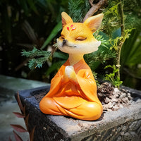 The Little Zen Fox in Orange, meditating on the edge of a planter