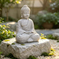 The Still Buddha seated on a flat stone among moss, gravel and greenery